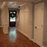 A view down the entry hall with custom block panel walls, and columns. The custom made front door is remant of the period design of the home. Can you find the hidden closet under the stairs?